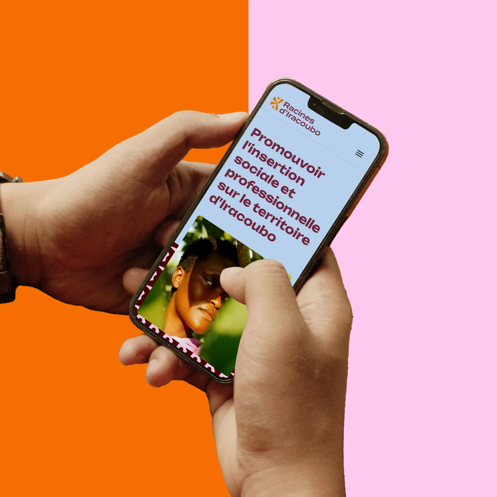 Le site de Racines d’Iracoubo sur un téléphone tenu à deux mains : « Promouvoir l’insertion sociale et professionnelle sur le territoire d’Iracoubo », sur fond orange et rose (mise en situation)
