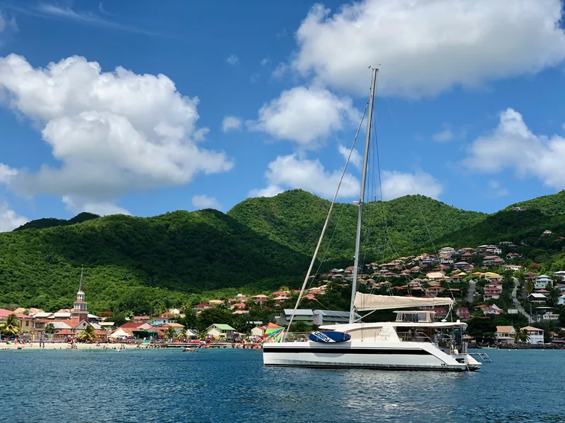A catamaran at anchor off a village, with its church steeple and green hills, in Martinique